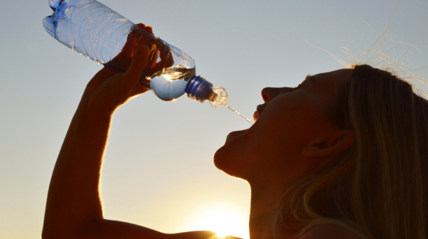 Silhouette,Of,A,Woman,Drinking,Water,From,Bottle,At,Sunset.
